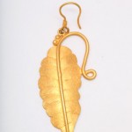 A gold leaf earring hanging from a hook.