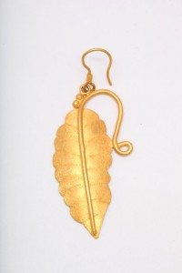A gold leaf earring hanging from a hook.