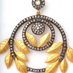 A gold and diamond earring with leaves hanging from the bottom.