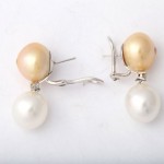 A pair of earrings with two pearls hanging from them.