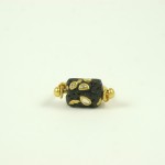 A black and gold bead is sitting on top of a white surface.