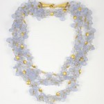 A necklace of three strands with gold beads and blue glass flowers.