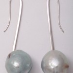 A pair of long silver earrings with large pearls.