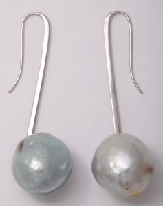 A pair of long silver earrings with large pearls.