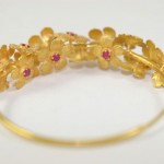 A gold bracelet with flowers and red stones.