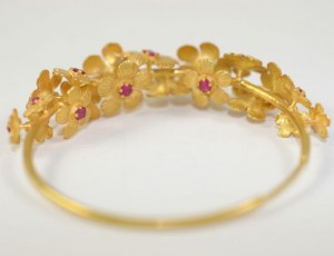 A gold bracelet with flowers and red stones.