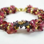 A close up of a bracelet with red and gold beads