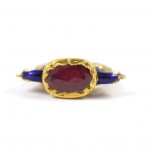 A gold ring with a red stone and blue stones.