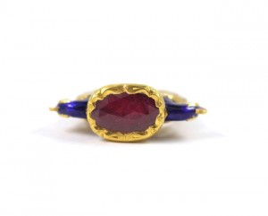 A gold ring with a red stone and blue stones.