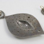 A metal leaf pendant with two earrings on the other side.