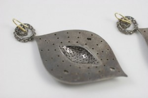 A metal leaf pendant with two earrings on the other side.