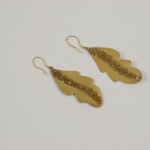 A pair of gold leaf earrings on a white surface.