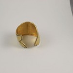 A gold plated cuff bracelet sitting on top of a table.