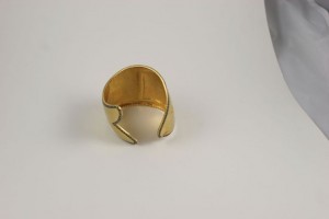A gold plated cuff bracelet sitting on top of a table.