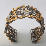 A metal bracelet with gold leaves on it.