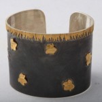 A metal bracelet with gold leaf on it.