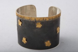 A metal bracelet with gold leaf on it.