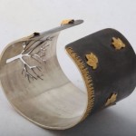 A silver bracelet with gold leaves on it.