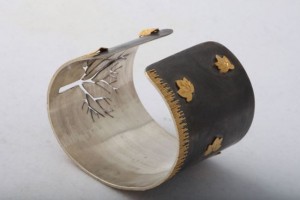 A silver bracelet with gold leaves on it.