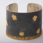 A metal bracelet with gold leaf design on it.