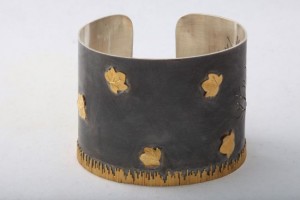 A metal bracelet with gold leaf design on it.