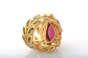 A gold ring with green and pink stones.