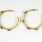 A pair of gold hoop earrings with bees on them.