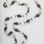 A long necklace of white beads and black metal leaves.