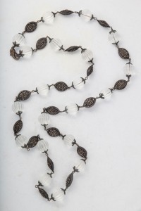 A long necklace of white beads and black metal leaves.