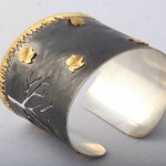 A silver and gold cuff bracelet with leaves.