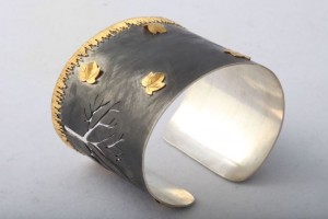 A silver and gold cuff bracelet with leaves.
