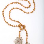 A long necklace with gold beads and a white flower.