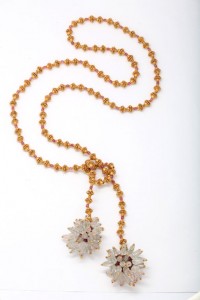 A long necklace with gold beads and a white flower.