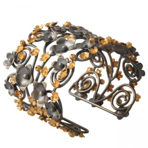 A metal bracelet with gold flowers and swirls.