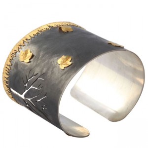 A silver and gold cuff bracelet with trees.