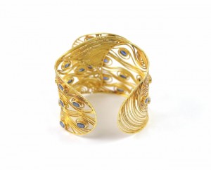 A gold bracelet with peacock feathers and blue stones.