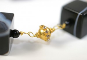 A close up of the gold bead on a black necklace