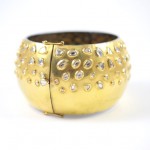 A gold bangle with clear stones on it.