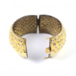 A gold bracelet with holes and rivets.