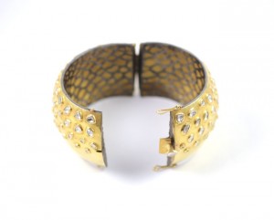 A gold bracelet with holes and rivets.