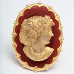 A gold and red brooch with a woman 's face.