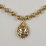 A gold necklace with a large pendant on top of it.