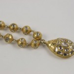 A gold necklace with a large pendant and small beads.