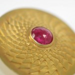 A close up of the top of a gold object with a red stone.