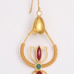 A gold earring with red and green stones.