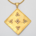 A gold pendant with four white stones on it.