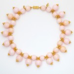 A pink necklace with gold beads and bows.