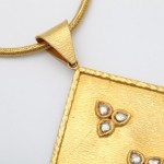 A gold necklace with a square shaped pendant.